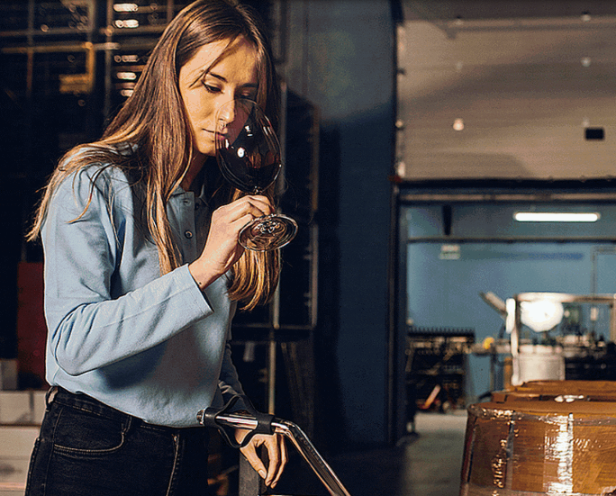 Woman tasting wine from a glass next to a wine barrel