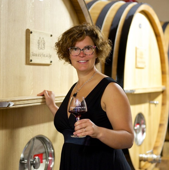 woman holding a glass of wine in front of wine barrel