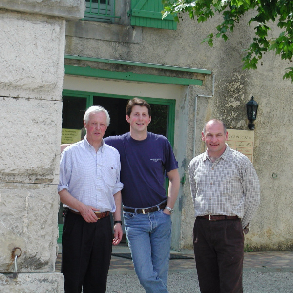 three men face camera in front of old stone building